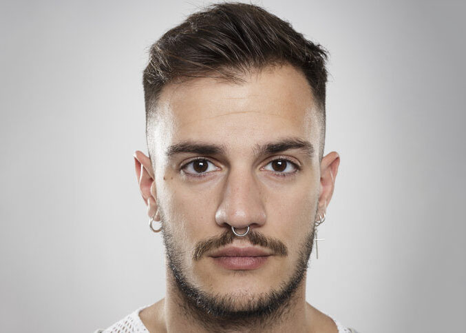 Portrait of a young man with piercings and earrings against neutral background